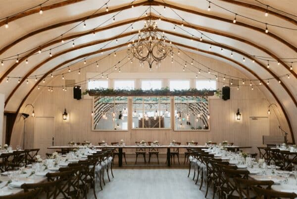 Rustic wedding barn venue with chandeliers, string lights, and elegantly set tables for a charming reception.