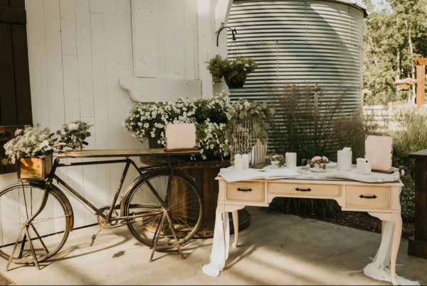 Rustic outdoor celebration setup with vintage bike, flowers, and elegant table setting under sunny skies.