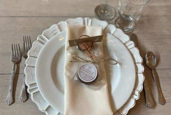 Elegant table setting with white plate, cream napkin, and glassware on rustic wooden table. Perfect for weddings or events.